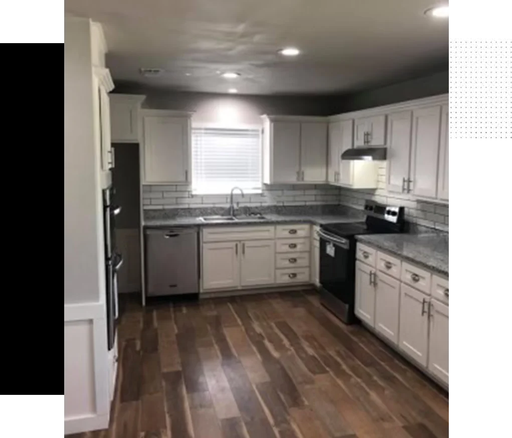 A kitchen with white cabinets and wood floors.